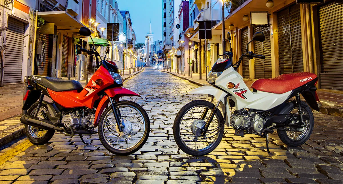 Motocicletas Pop 110i ES Branco Ross White e Pop 110i ES Vermelho - Maceio Red em pose na rua de paralelepípedo