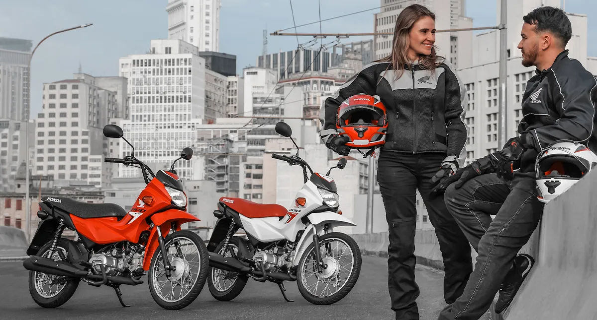 Mulher e Homem conversando com seus capacetes em mãos e motocicletas Honda Pop 110i ES ao fundo