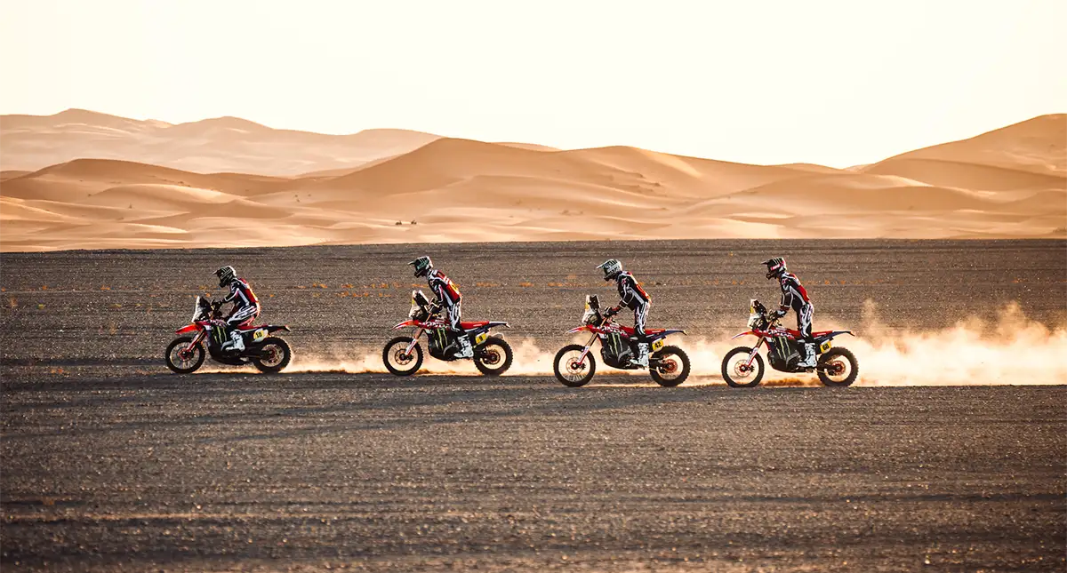 Quatro motos de rally cruzando o deserto em fila
