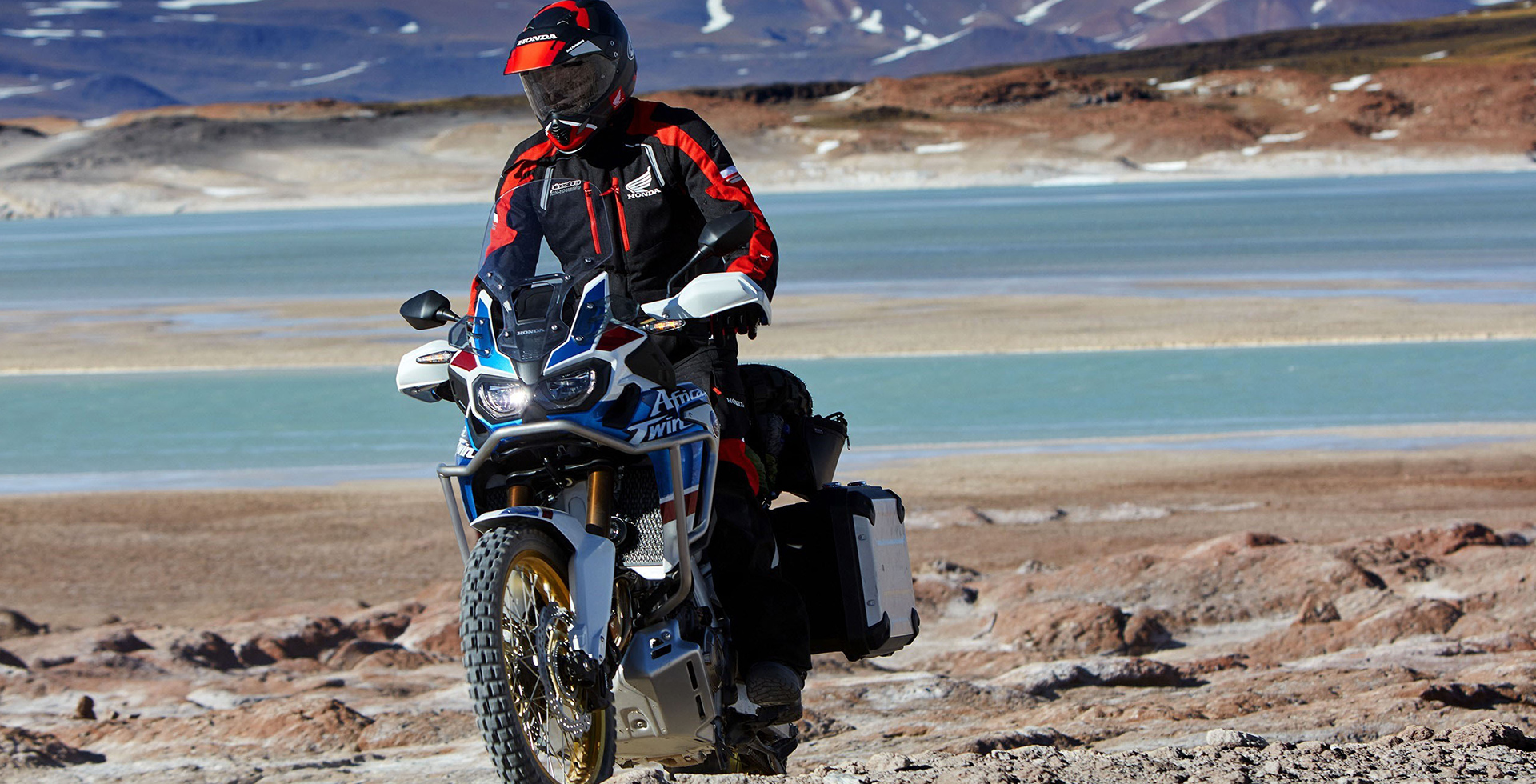 Homeme em moto Honda Africa Twin em paisagem com pedras e lago usando capacete Honda