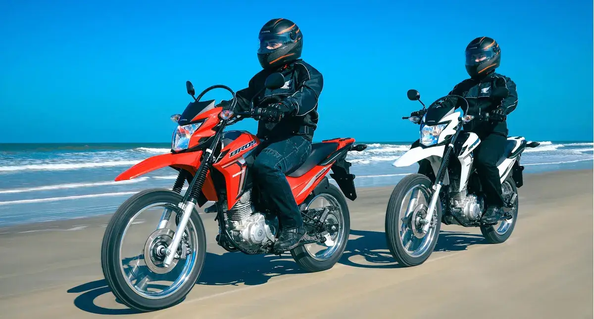 Dois pilotos em moviemnto em suas Motos Honda NXR 160  Bros uma vermelha e outra branca a beira mar