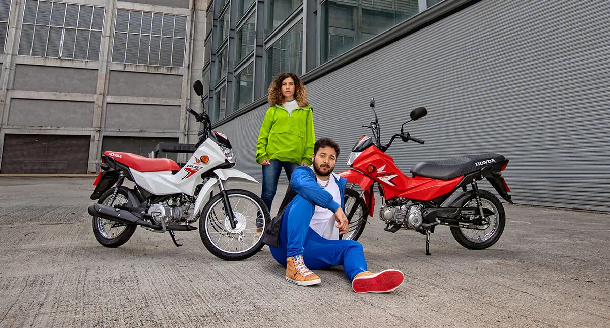 Homem e Mulher posando para uma fotografia entre as motocicletas Pop 110i ES Branco Ross White e Pop 110i ES Vermelho - Fighting Red