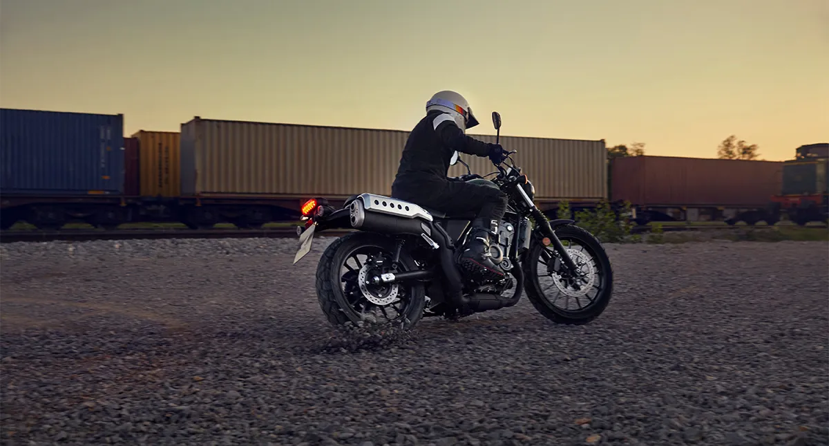 Piloto na Moto CL 500 com containers ao fundo