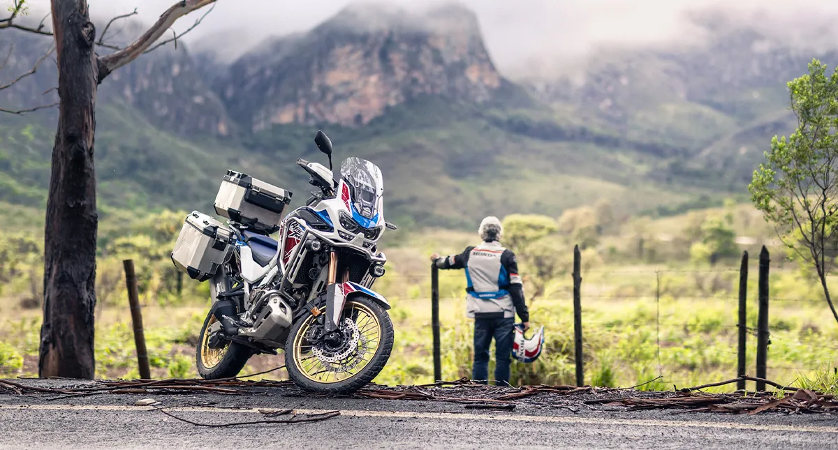 CRF 1100L a Africa Twin estacionada a beira da estrada e piloto ao fundo com capacete em mãos admirando a paisagem da natureza
