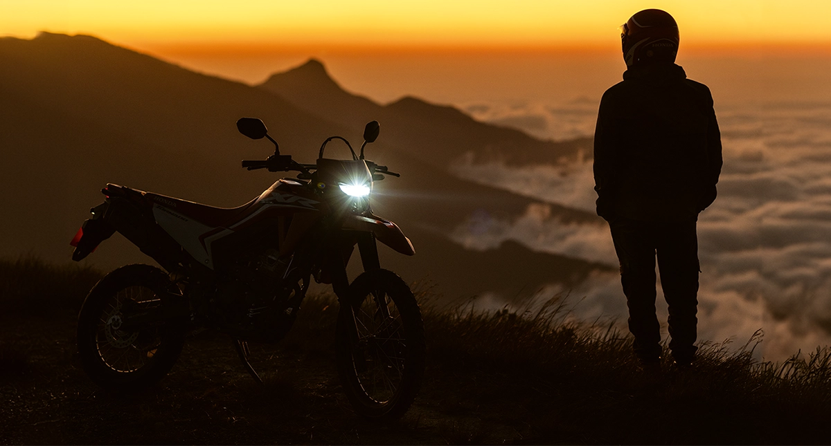 Motocicleta Honda XR 300L Tornado com farol aceso e piloto olhando pôr do sol