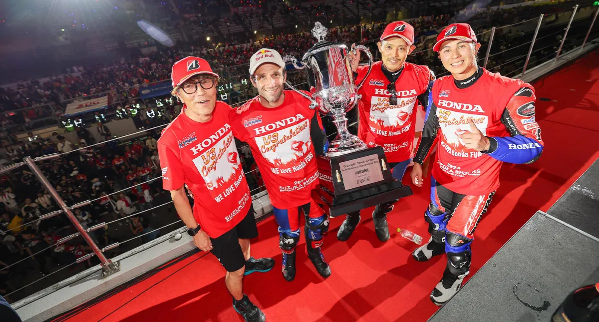 Pilotos com roupas da Honda vermelha e troféu em mãos