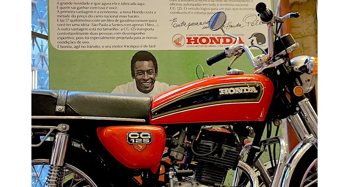 Motocicleta Honda 125 em exibição com um painel informativo ao fundo
