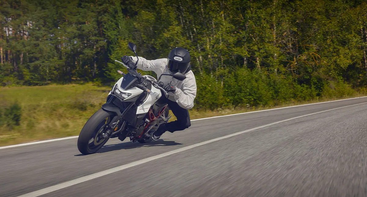 Moto fazendo curva em estrada com mata