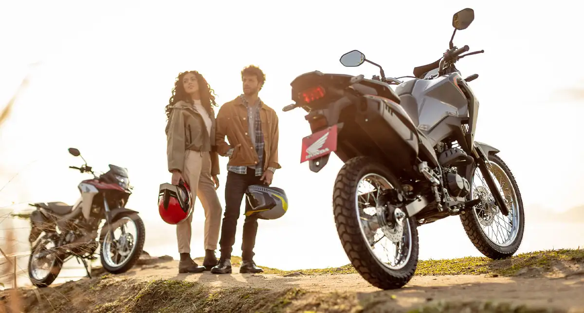 Mulher e homem com capacete na mão entre duas motocicleta XRE 190 