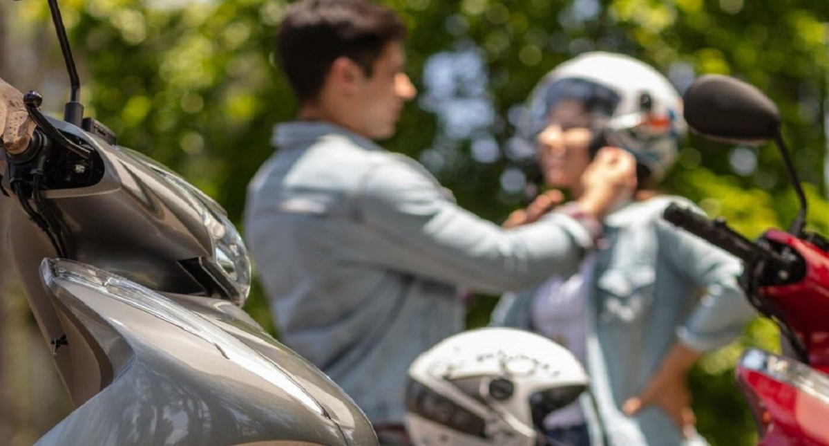 Homem ajustando capacete Honda em cabeça de mulher com motos a frente