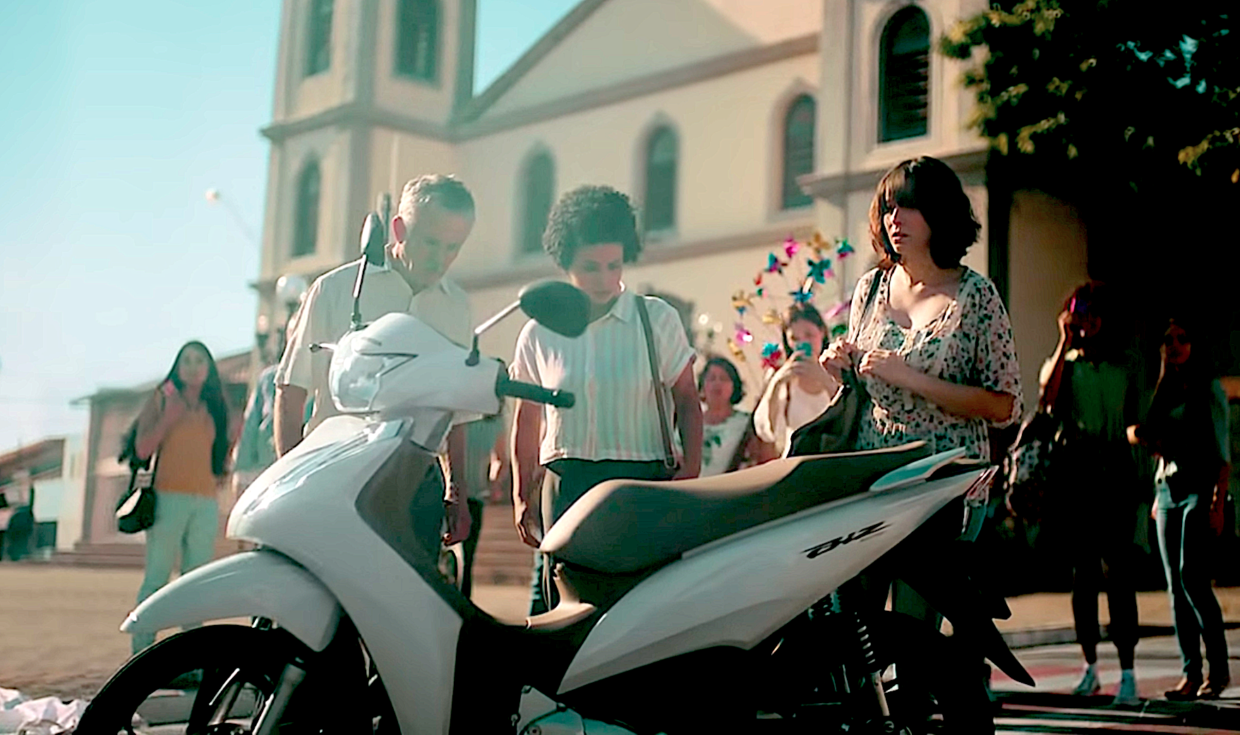 Homem, Mulher e Menino olhando para Moto Honda Biz Branca