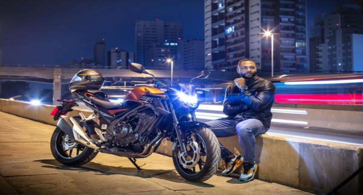 Homem sentado ao lado de moto Honda CB 500F com farol acesso