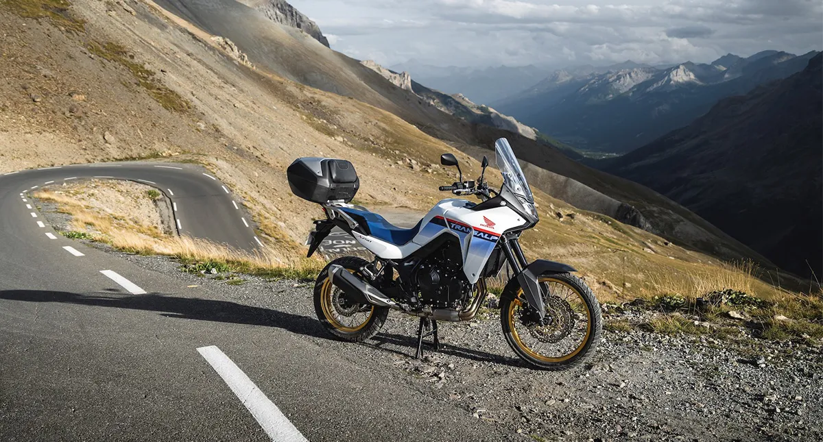 Moto Honda XL 750 Transalp estacionada na estrada com morro ao fundo