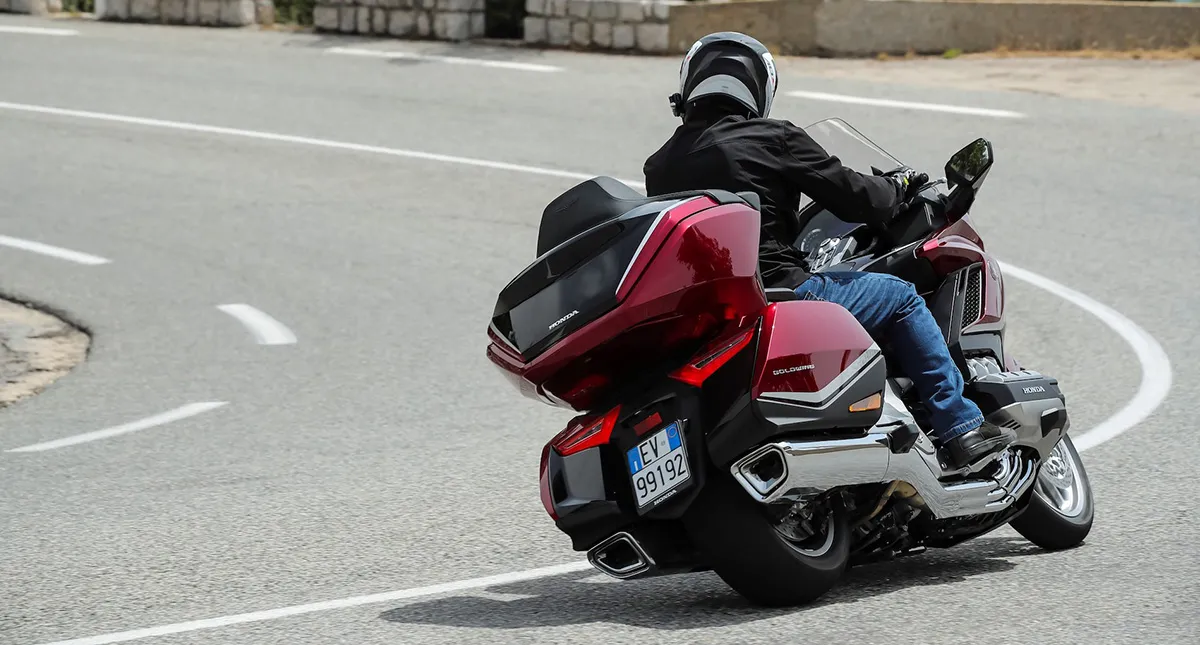 Piloto na estrada fazendo curva para a esquerda com sua Moto Honda GL 1800 Gold Wing Tour vermelha