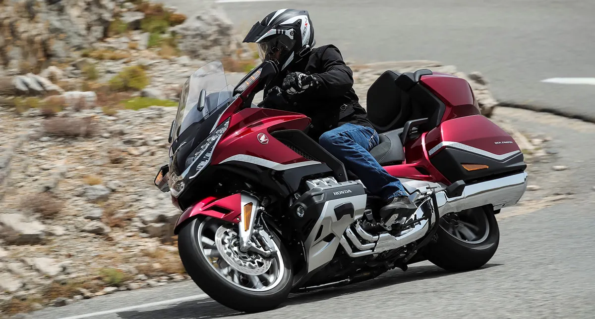 Piloto na estrada fazendo curva em sua Moto Honda GL 1800 Gold Wing Tour vermelha