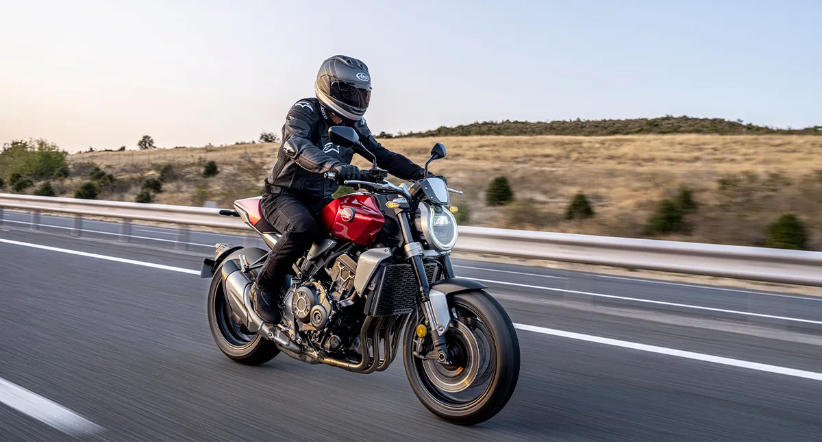 Homem de Jaqueta Preta Pilotando Moto Honda CB 1000R Vermelha em Estrada