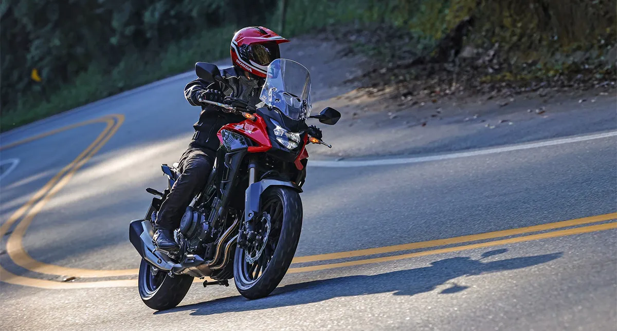 Homem em moto Honda CB 500X vermelha fazendo curva