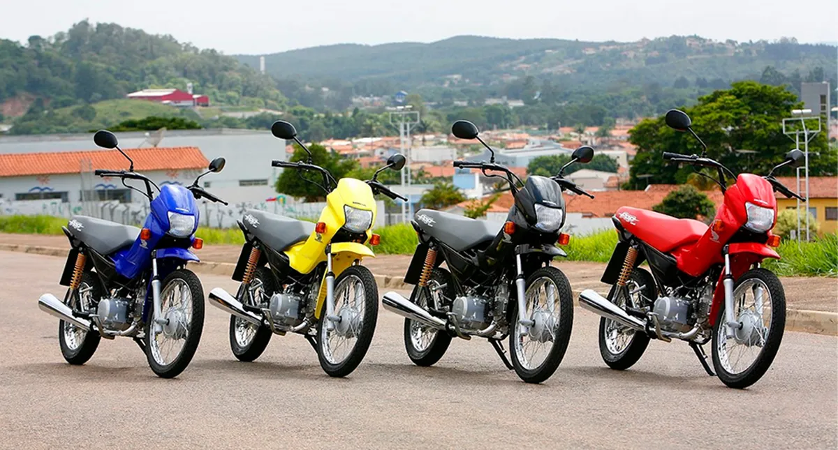 Quatro motos Honda Pop 100 modelo 2007 estacionadas, nas cores azul, amarelo, preto e vermelho