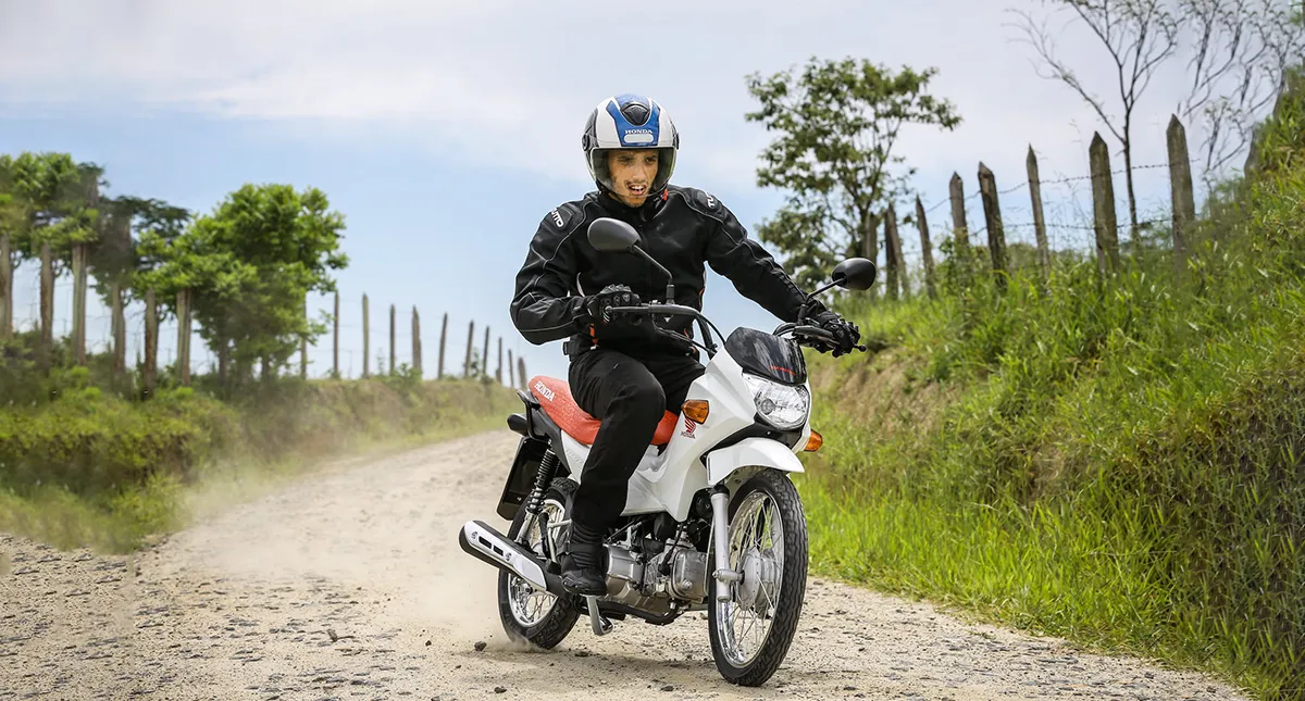 Piloto com a moto Honda Pop 110i andando em estrada de terra