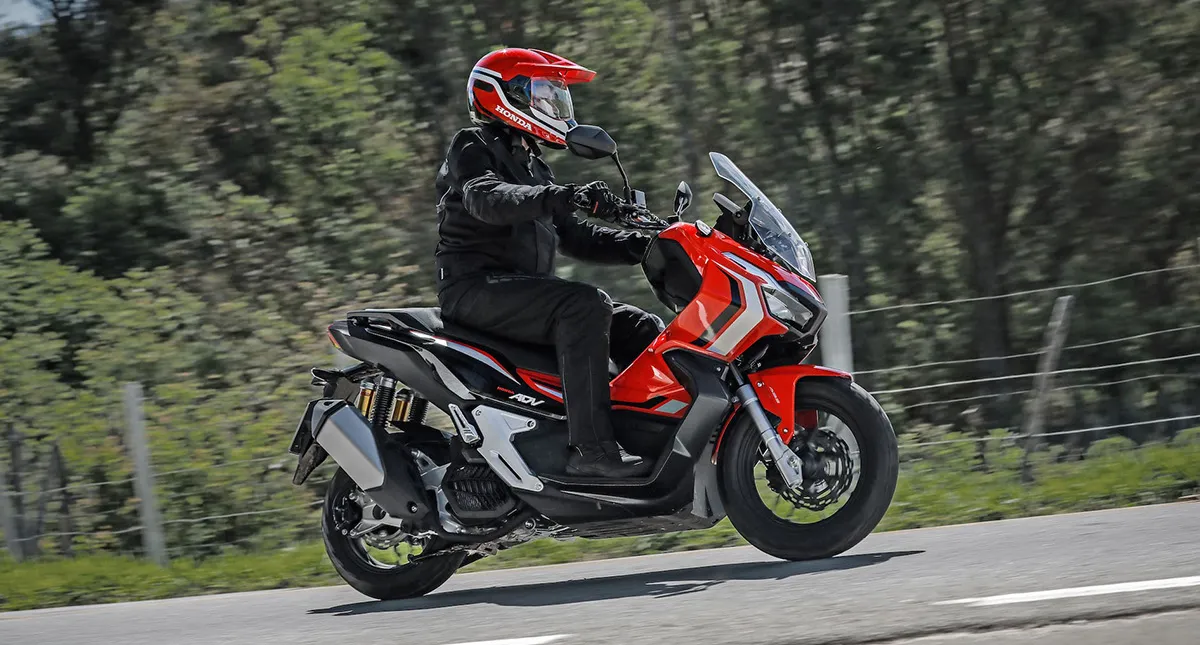 Piloto com sua Scooter Honda ADV vermelha na estrada