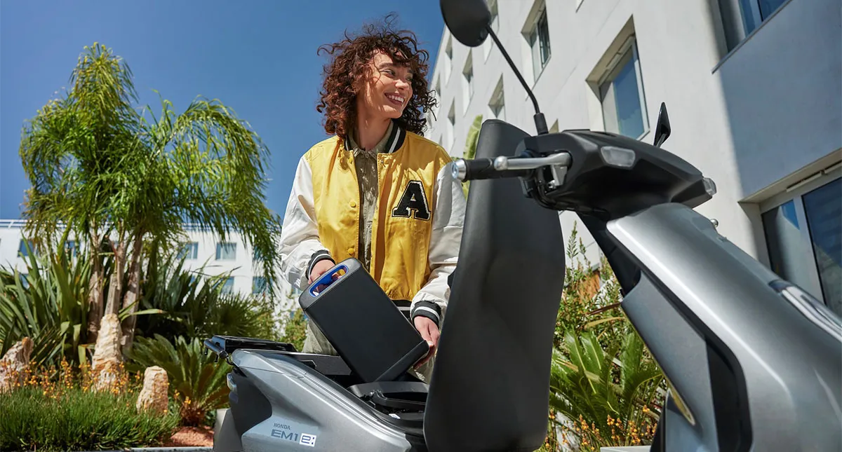 Mulher colocando a bateria em sua Honda EM1 e