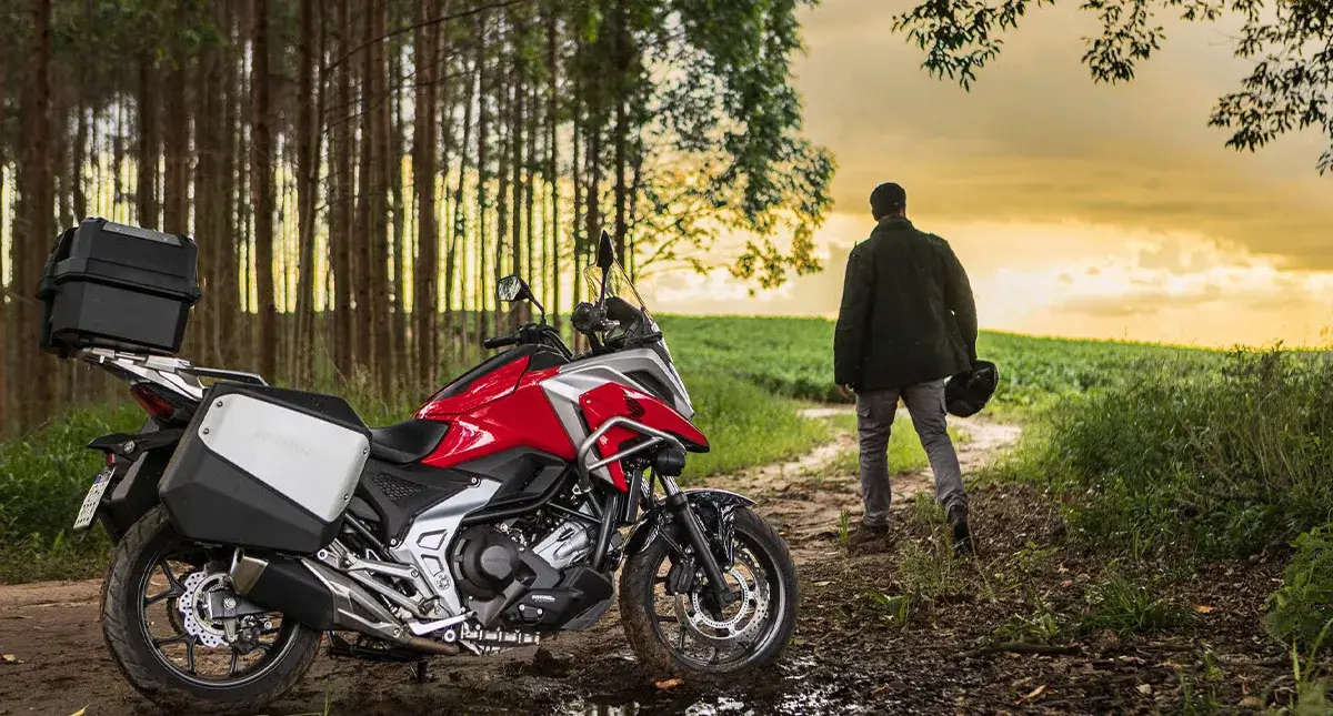 Homem em pé olhando paisagem segundando capacete ao lado da Moto Honda NC 750 com DCT