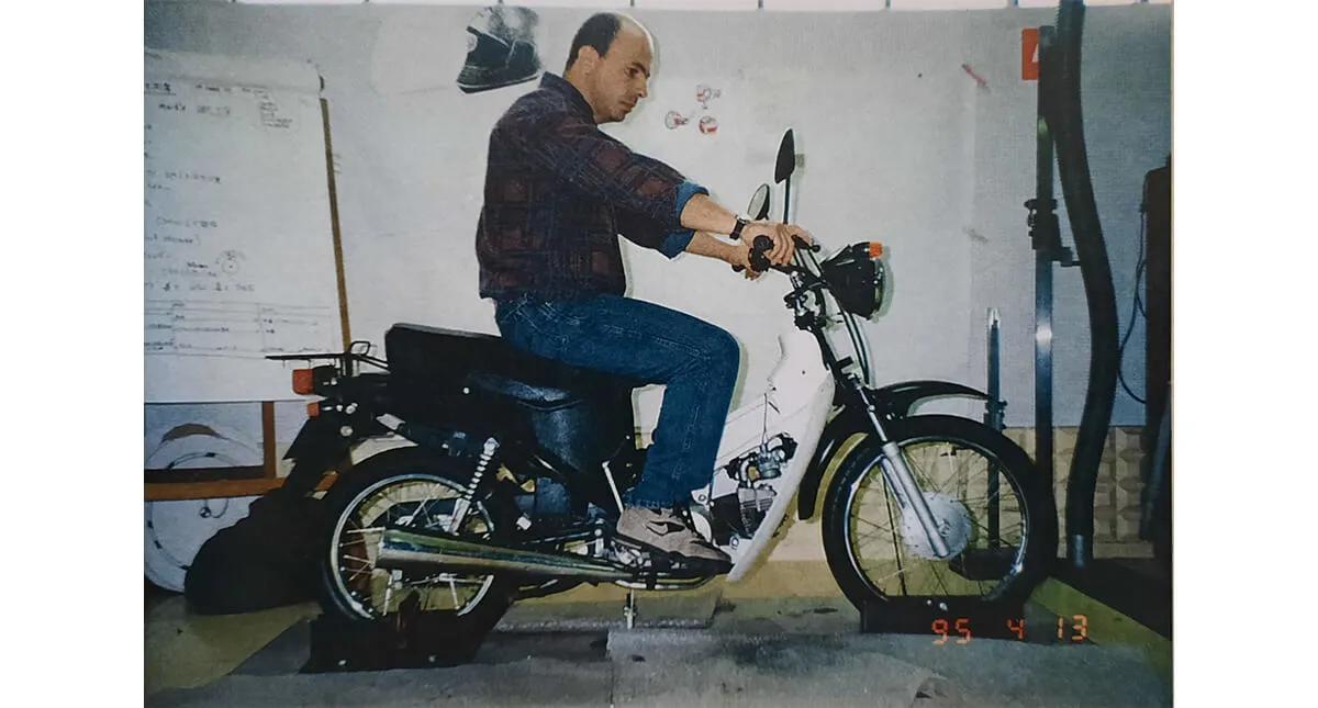 Fabricação da Honda Biz colaborador sentado na moto com quadro do projeto ao fundo