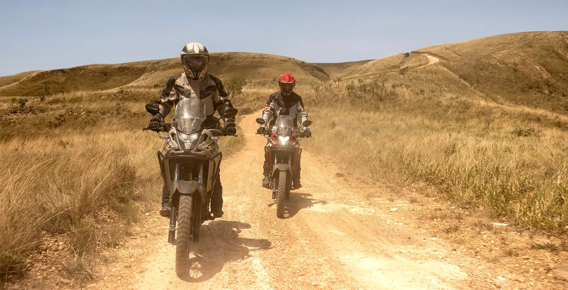 Dois pilotos lado a lado em estrada de terra pilotando Honda Sahara 300