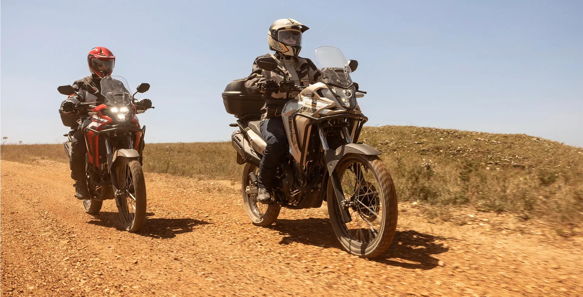 Dois pilotos lado a lado em estrada de terra pilotando Honda Sahara 300