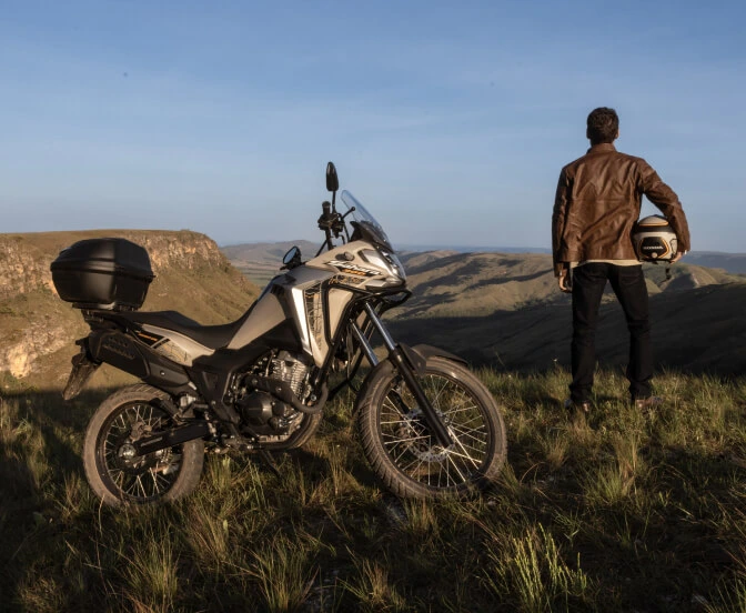 Homem segurando capacete e olhando horizonte ao lado de moto Honda Sahara 300