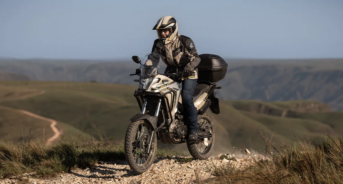 Mulher branca em moto Honda Sahara 300 Adventure em trilha de pedra