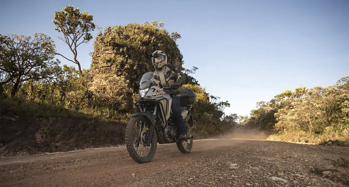 Piloto em moto Honda Sahara 300 cinza em estrada de areia