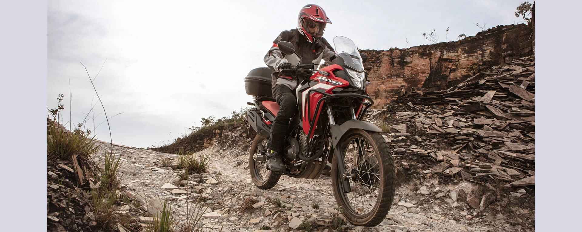 Piloto em moto Honda Sahara 300 vermelha em estrada de areia usando a tecnologia do câmbio de 6 marchas
