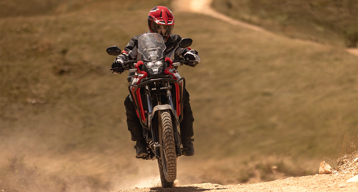 Piloto em moto Honda Sahara 300 vermelha em estrada de areia