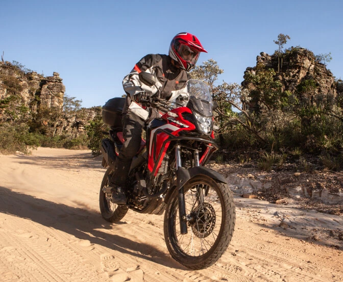 Piloto em moto Honda Sahara 300 vermelha em estrada de areia