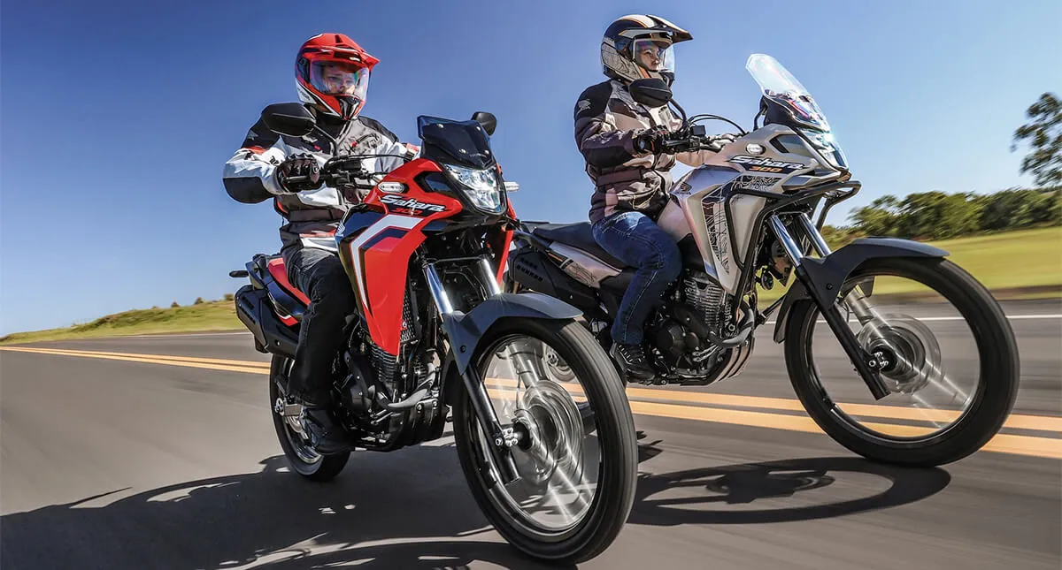 Casal em Estrada de Asfalto com Motocicleta Honda Sahara 300 Vermelha e Outra Prata