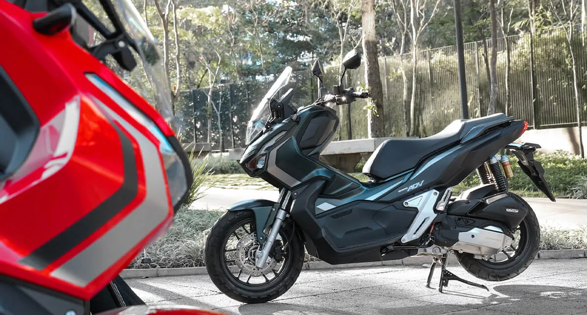 Detalhe do Farol da ADV Vermelha e Motocicleta Honda ADV Preta ao Fundo