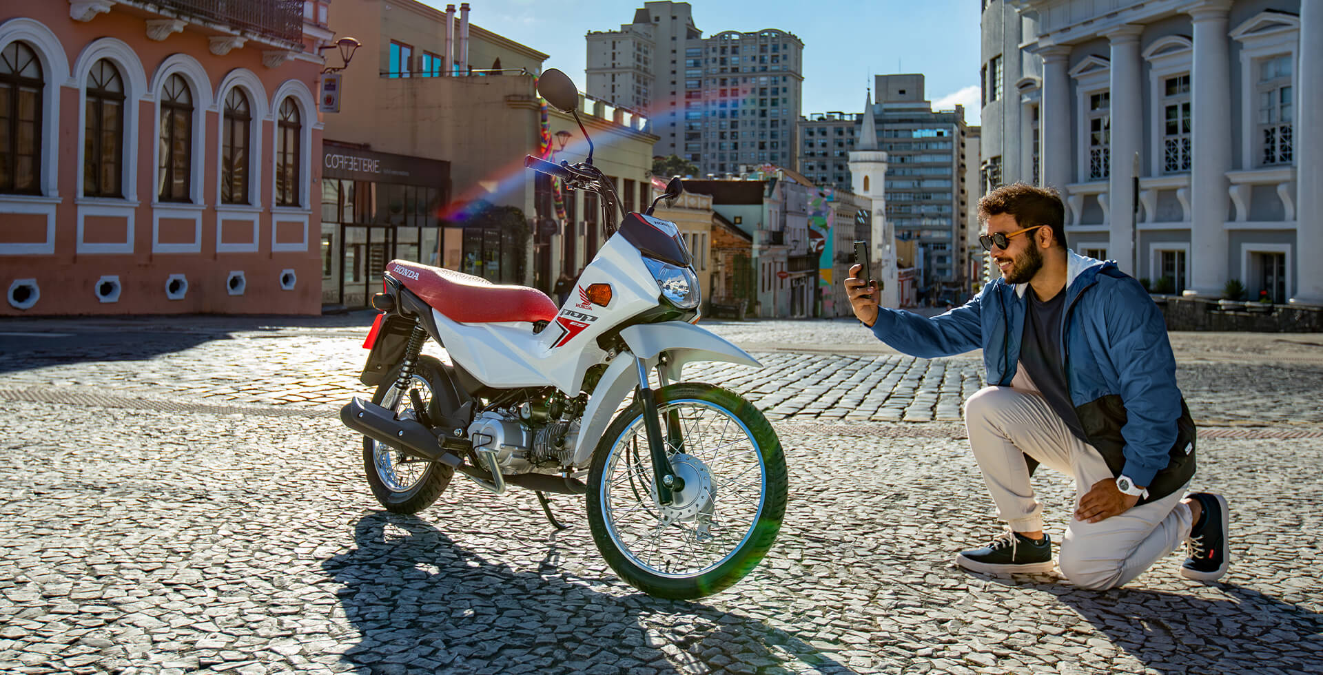 Homem Agachado na Rua e Tirando foto da Moto Honda Pop 110i ES na cor Branco Ross White