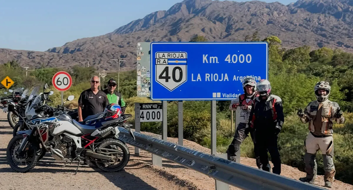 Pilotos ao lado da placa de la rioja 4000km em estrada da Argentina