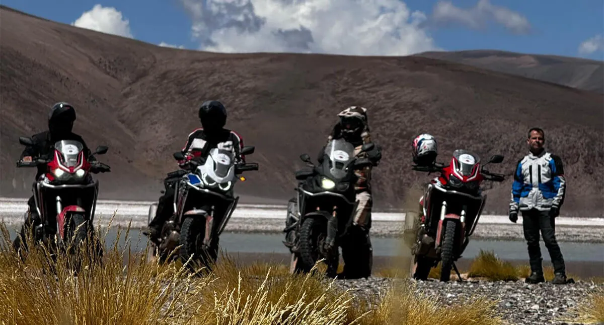 Pilotos lado-a-lado com suas motocicletas e andes atrás