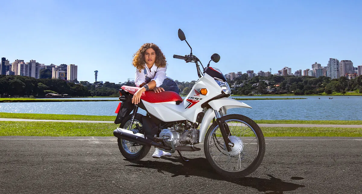 Mulher posando para câmera encostada no banco da motocicleta Pop 110i ES Branco Ross White 