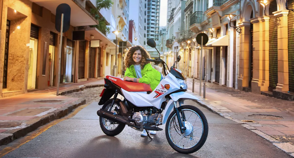 Mulher sorrindo e posando para câmera encostada no banco da motocicleta Pop 110i ES Branco Ross White 