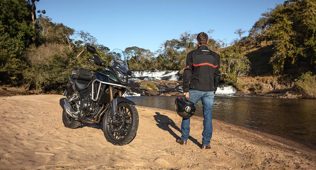 Piloto ao lado de sua motocicleta Honda CB 500X admirando de um rio