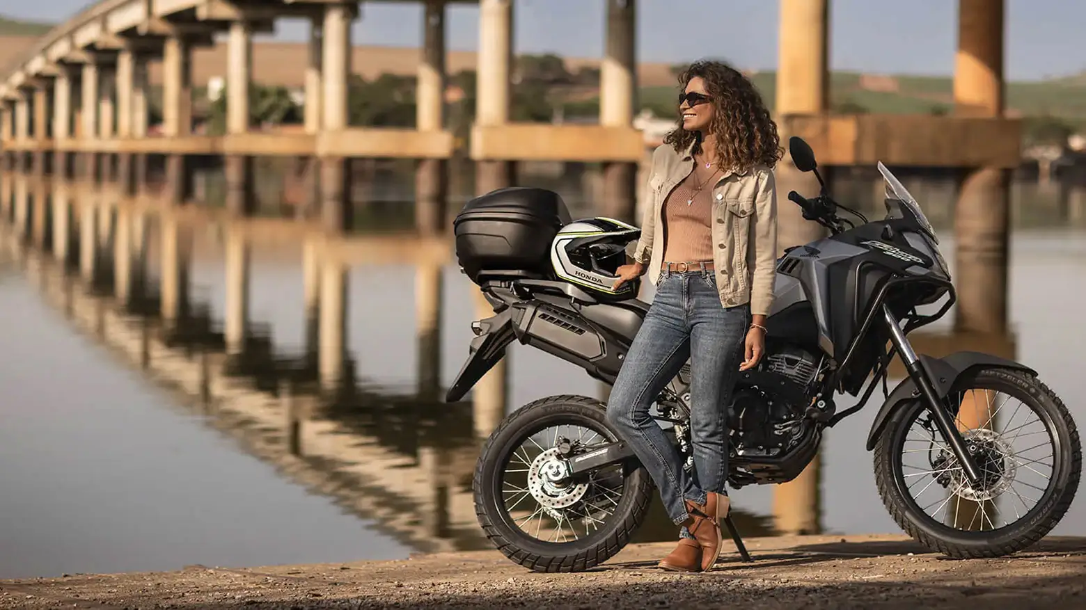 Mulher encostada em Honda Sahara 300 Standard com capacete no banco 