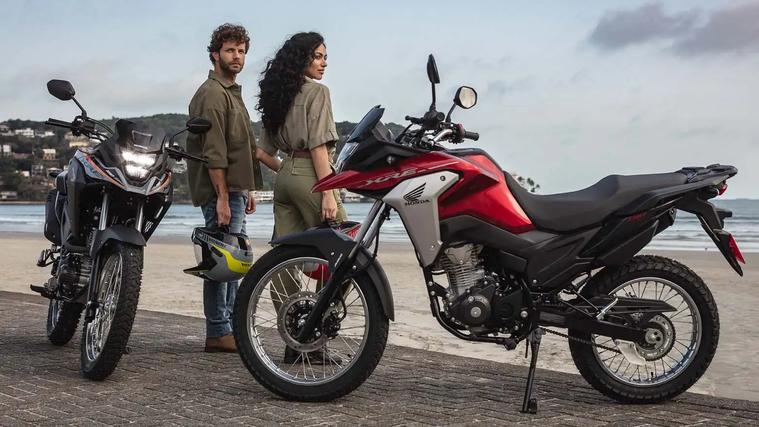 Homem e mulher olhando o horizonte da praia ao lado das Motos Honda XRE 190