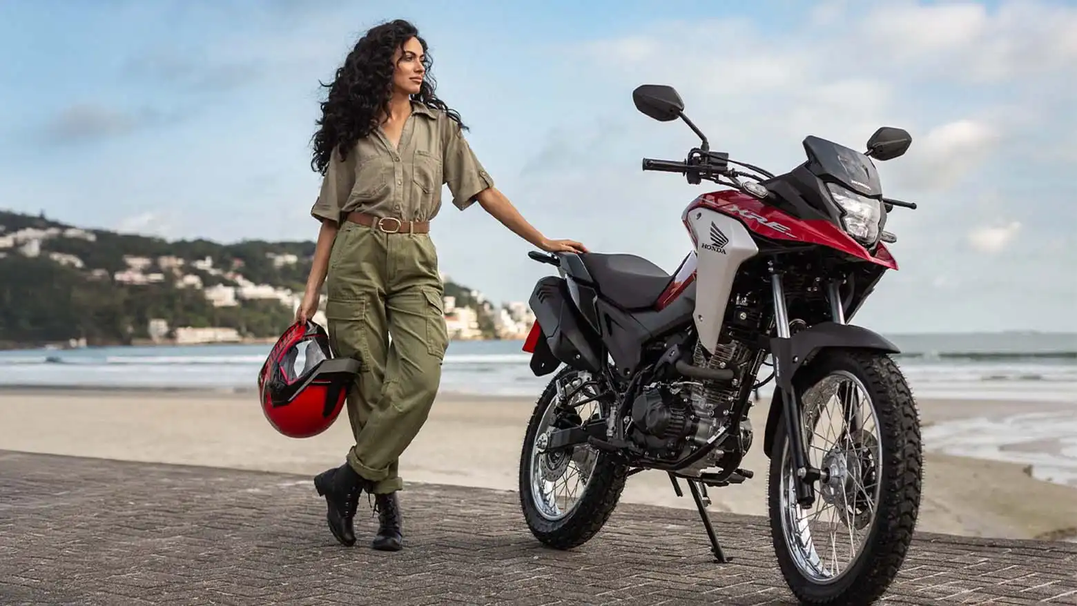 Mulher fazendo pose e segurando capacete ao lado da Moto Honda XRE 190