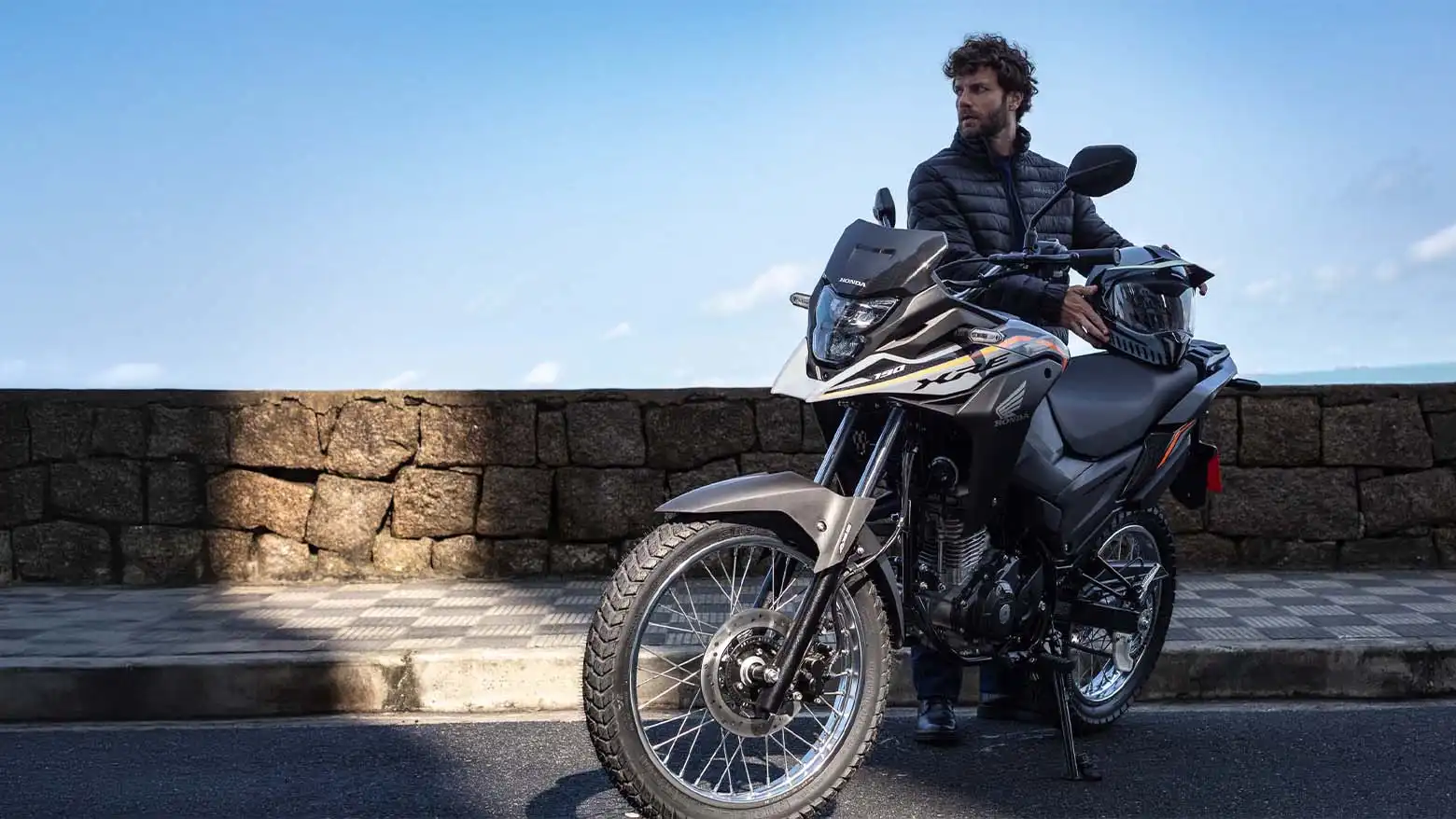 Homem fazendo pose e apoiando capacete no banco da Moto Honda XRE 190