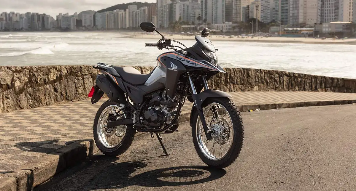 XRE 190 cinza em rua de asfalto com cidade litoranêa ao fundo