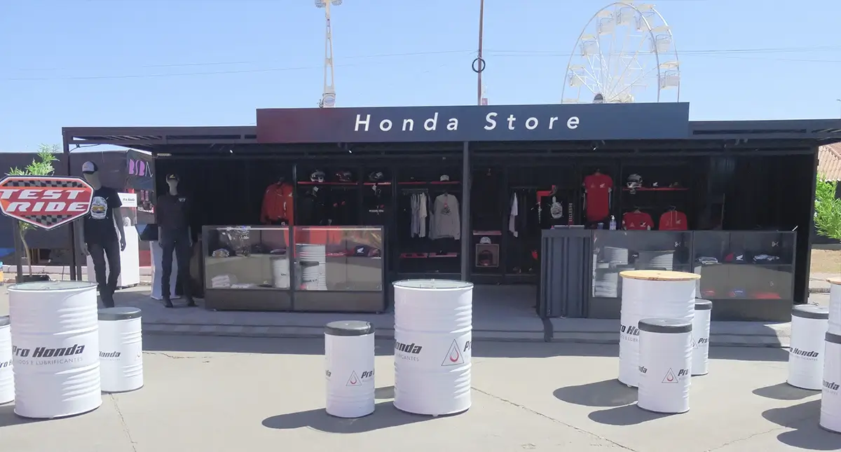 Vista frontal da loja Honda Store no Capital Moto Week 2025, com mesas brancas ao ar livre e estrutura preta ao fundo