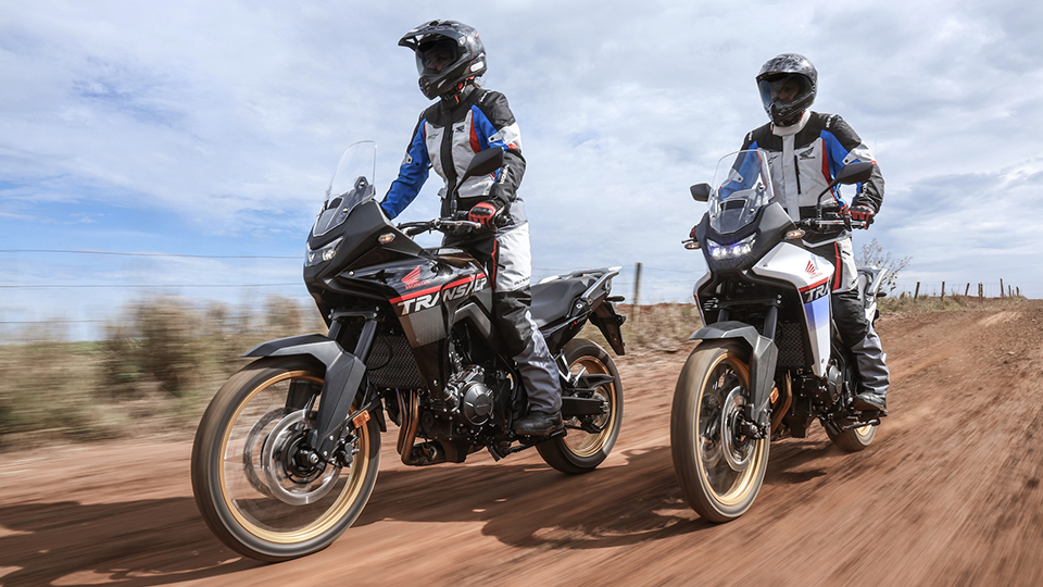 Dois motoqueiros pilotando Hondas Transalp em estrada de terra 